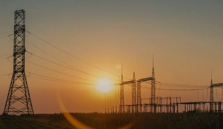 Power lines stretch across the golden sunset, silhouetted against the vibrant sky